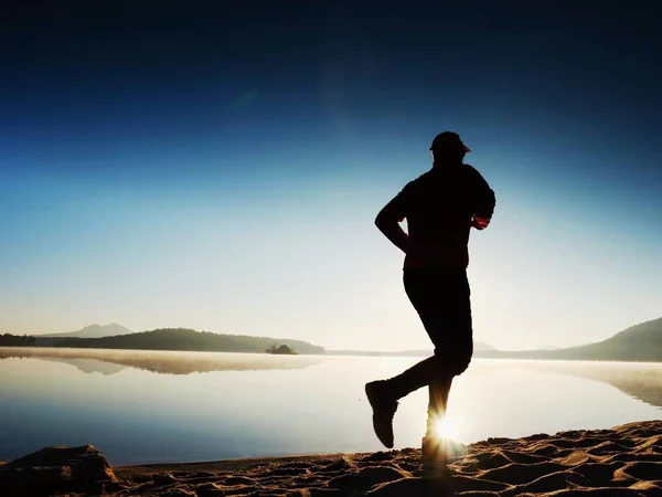 Man uit te oefenen en rekken op het lake strand bij zonsopgang. Gezonde levensstijl. Alleen jonge fitness man uitoefenen op ochtend strand — Stockfoto