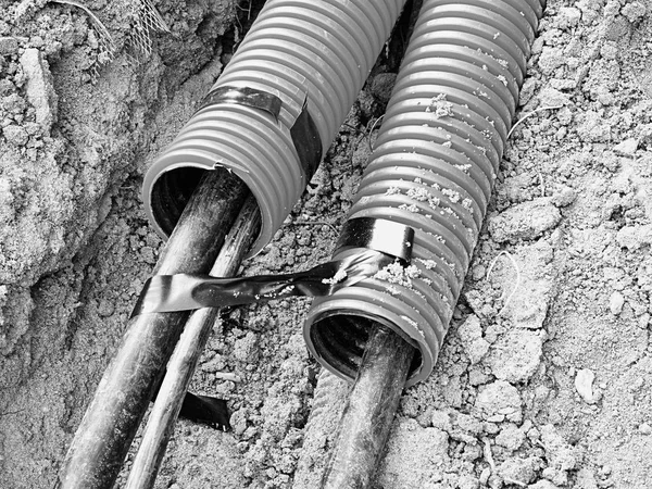 Excavation of trench with black cables in protective HDPE tube. Lines of metallic and fiber optic wires. — Stock Image Excavation of trench with black cables in protective HDPE tube. Lines of metallic and fiber optic wires. Stock Image