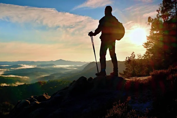 Silhueta de caminhante sozinho com postes na mão. Turista com mochila desportiva stand no ponto de vista rochoso acima do vale enevoado. Alvorada de primavera ensolarada em montanhas rochosas . — Fotografia de Stock