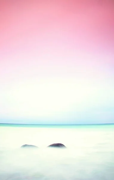 Ambiente romántico en la mañana tranquila en el mar. Grandes rocas que sobresalen del suave mar ondulado. Horizonte rosa —  Fotos de Stock