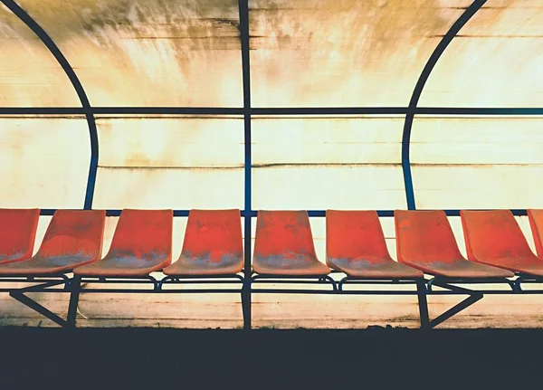 Sedili in plastica vintage sulla panchina dei giocatori dello stadio all'aperto, sedie con vernice usurata sotto il tetto giallo . — Foto Stock