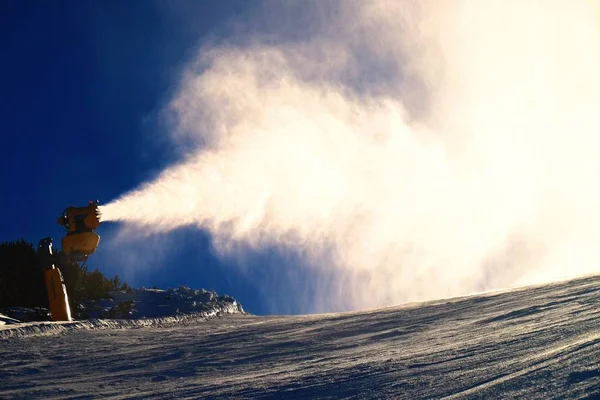 Σκιέρ κοντά ένα κανόνι χιόνι φτιάχνοντας χιόνι σκόνη. Άλπεις χιονοδρομικό κέντρο. — Φωτογραφία Αρχείου