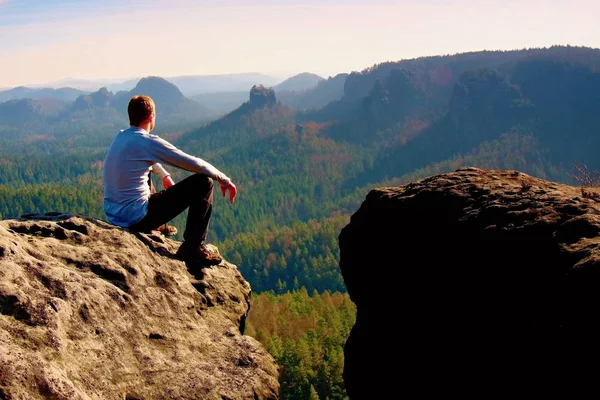 Young man in black sportswear is sitting on cliff edge and looking to misty valley bellow — Stock Photo, Image