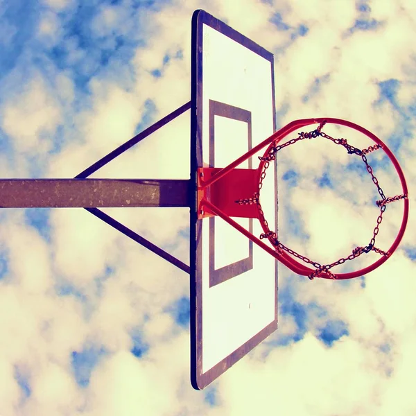 Antiguo tablero de baloncesto descuidado con aro oxidado sobre la cancha de la calle. Cielo nublado azul en bckground. Filtro retro — Foto de Stock