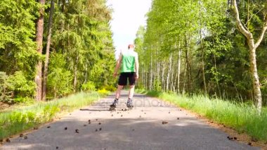Arka görüş için yeşil çalışan singlet satır içi patenci. Ormanın içinde düzgün asphal üzerinde açık paten. Açık tenli adam tekme çam kozalakları yolda, ağırlık merkezi hareketli içine.