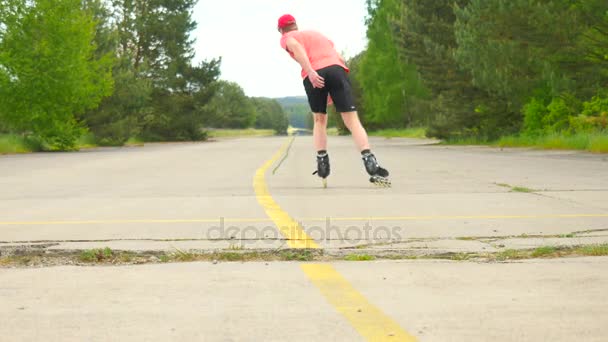 Rear view to inline skater in green running singlet . Outdoor inline skating on smooth asphalt in the forest. Light skin man is jumping on the road, moving with center of gravity. — Stock Video