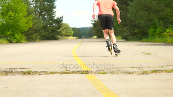 Rear view to inline skater in green running singlet . Outdoor inline skating on smooth asphalt in the forest. Light skin man skating on the road, moving with center of gravity. — Stock Video