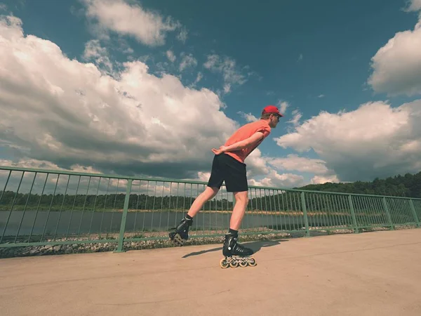 Blick von hinten auf Inline-Skater in rotem T-Shirt und schwarzer Hose, die auf der Brücke Schlittschuh laufen. Inlineskating im Freien — Stockfoto