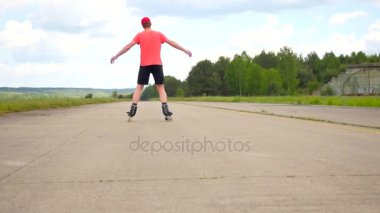 Yetişkin satır içi skater bir dalga. Pratik patenci tadını çıkarın paten içinde germe. Adam güneş gözlüğü, hafif kırmızı tişört ve siyah pantolon. Güzel güneşli yaz günü doğa skate Park