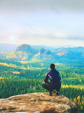 Açık kıyafetler üzerinde kırık kayalık empires oturup siyahlı adam. Sonbahar Derma landcape.