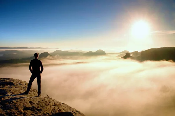 Escursionista in nero si trova sulla roccia abve valle entro l'alba e guardare al sole. Bellissimo momento il miracolo della natura — Foto Stock