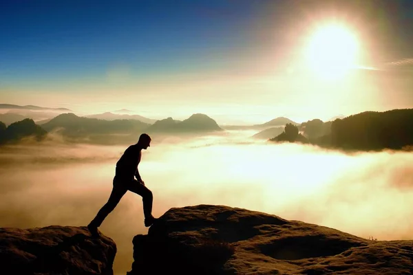 Crazy hiker in black is jumping between the rocky peaks. Wonderful daybreak in rocky mountains, heavy mist in deep valley. Miracle of nature — Stock Photo, Image