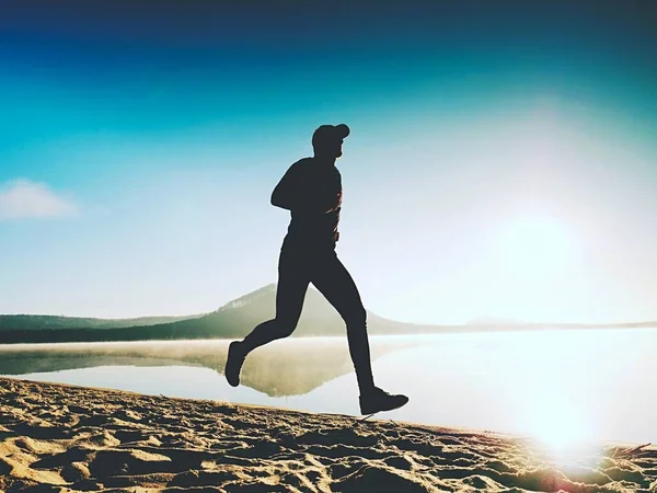 Hombre corriendo a la orilla del mar al anochecer. Atleta corredor corriendo a la orilla del mar. Sportsman silueta fitness —  Fotos de Stock