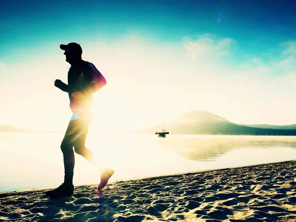 Hombre corriendo a la orilla del mar al anochecer. Atleta corredor corriendo a la orilla del mar. Sportsman silueta fitness — Foto de Stock