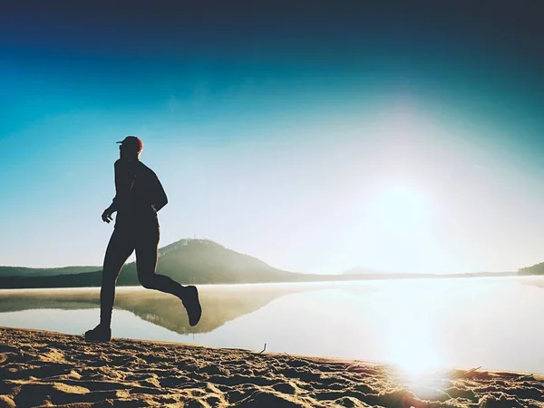 Gezonde levensstijl. Hoog jongeman runner draait op zonsopgang aan zee. Man sprong in zand — Stockfoto