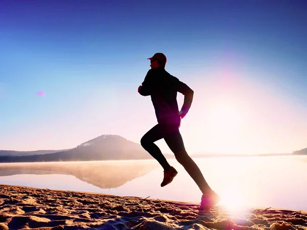 Estilo de vida saudável. O jovem corredor corre ao nascer do sol à beira-mar. Homem salta na areia — Fotografia de Stock