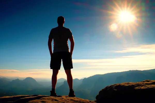 Einsamer Wanderer in schwarzen Hosen steht auf Felsen und wacht über das neblige Morgental zur Sonne. — Stockfoto