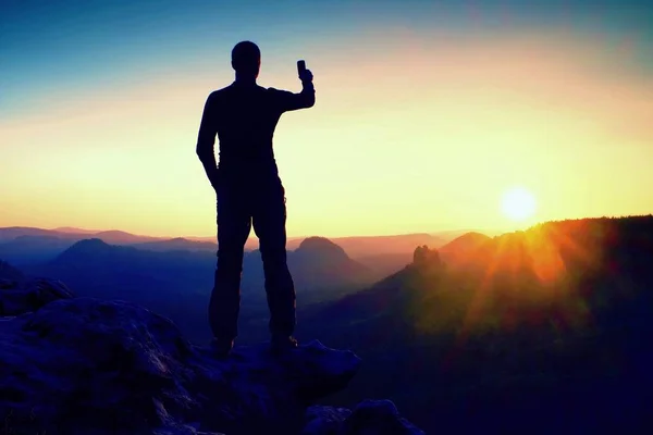 Selfie mania. Vysoký muž tramp je s selfie Foto chytrý telefon na vrcholu hory při východu slunce. — Stock fotografie