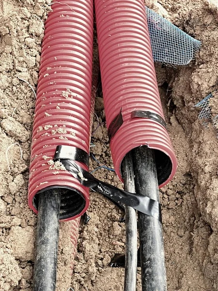 Excavation de tranchée avec des câbles noirs dans un tube de protection en PEHD. Lignes de fils métalliques et de fibres optiques . — Photo