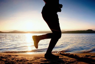 Gün batımında eğitim. Göl kıyı şeridi boyunca yola koşucu silüeti.