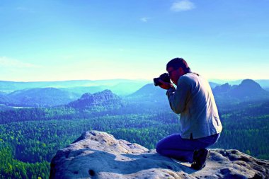 Siyah saçlı adam fotoğraf büyük ayna kamera dağ tepe üzerinde boynundaki güneş doğarken alıyor.