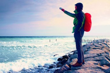 Fiyatı iskelesi fotoğraf sabah deniz üzerinde. Turist ile akıllı telefon elinde, kırmızı yağmurluk sırt çantalı. Harika sabah 
