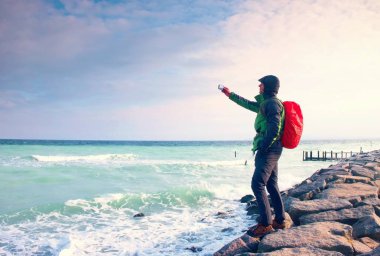 Fiyatı iskelesi fotoğraf sabah deniz üzerinde. Turist ile akıllı telefon elinde, kırmızı yağmurluk sırt çantalı. Harika sabah 