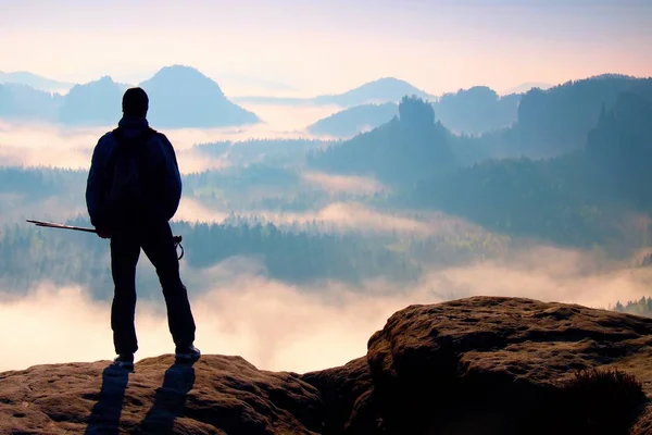 Dimmig dag i Klippiga bergen. Silhuett av turist med stolpar i handen. Vandrare stå på rocky synvinkel ovan misty valley. — Stockfoto