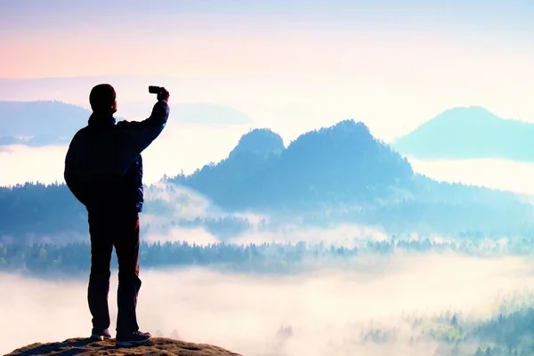 Turista alto está tomando selfie no pico acima do vale. Fotografia de telefone inteligente — Fotografia de Stock