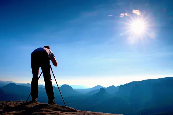 摄影爱好者留在三脚架上悬崖和思维。在下面的美丽山谷梦幻般顽固景观，蓝色朦胧日出 — 图库照片