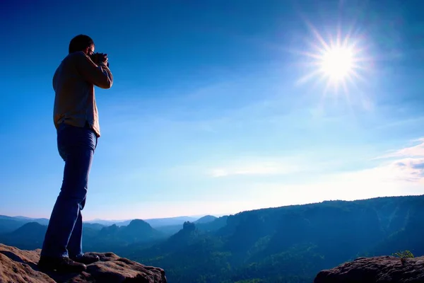 Profesionální fotograf pořizuje fotografie s zrcadlový fotoaparát na útesu skály. Zasněný zamlžená krajina, horké slunce nad — Stock fotografie