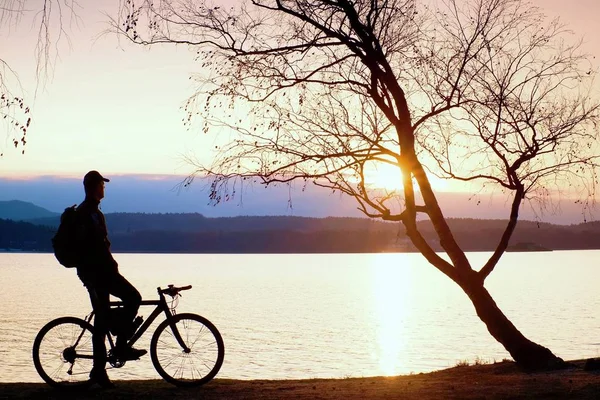 Jeune silhouette cycliste sur fond bleu ciel et coucher de soleil sur la plage. Fin de saison au lac . — Photo