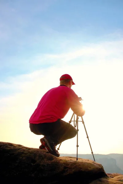 Photographerin chaqueta roja y gorra de béisbol roja estancia con la cámara en el trípode en el acantilado y el pensamiento. Paisaje de ensueño . —  Fotos de Stock