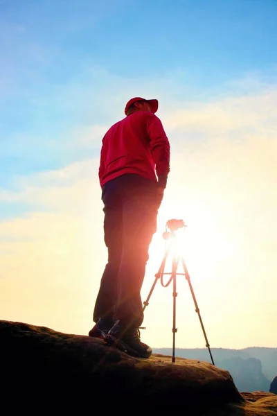 El fotógrafo se queda con el trípode en el acantilado y pensando. Paisaje de ensueño, amanecer nublado naranja en un hermoso valle — Foto de Stock