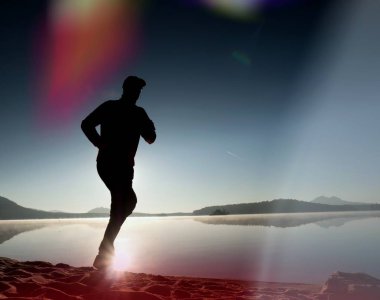  egzersiz ve göl kumsalda güneş doğarken uzanan bir adam. Sağlıklı bir yaşam tarzı. Yalnız genç fitness adam egzersiz sabah kumsalda