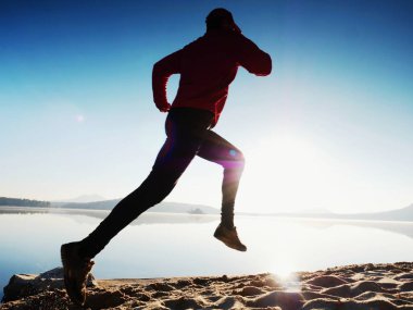 Egzersiz ve göl kumsalda güneş doğarken germe etkin adam silüeti.