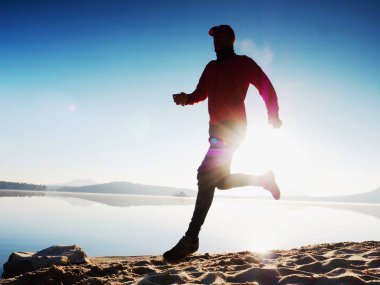 Egzersiz ve göl kumsalda güneş doğarken germe etkin adam silüeti.