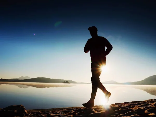 Człowieka, ćwiczenia i rozciąga się na plaży nad jeziorem o wschodzie słońca. Zdrowy styl życia. Sam młodych fitness mężczyzna poćwiczyć rano beach — Zdjęcie stockowe