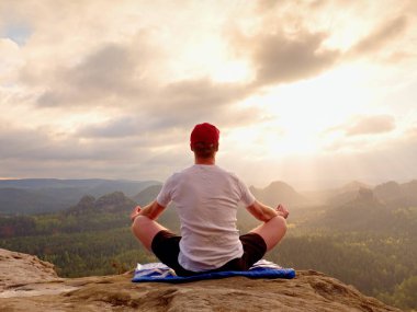 Yalnız adam pratik Yoga poz kayalık tepe üzerinde oturuyor. Adam puslu sabah içinde meditasyon yapmak 