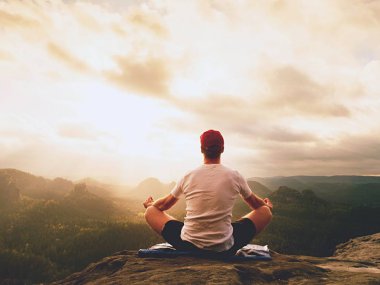 Yalnız adam practicin Yoga poz kayalık tepe üzerinde oturuyor. Adam puslu sabah içinde meditasyon yapmak 