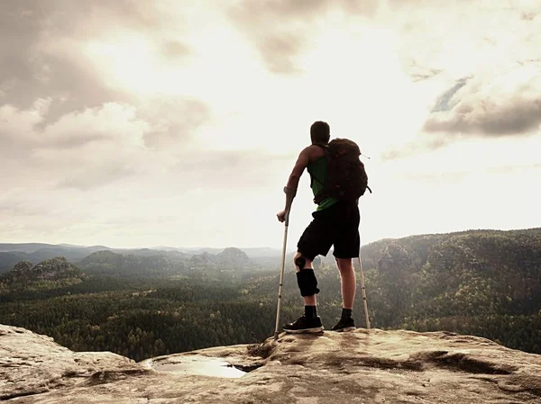 Doğada bir koltuk değneği olan adam. Kırık bacak koltuk değneği ile turist. Yaralı bacak bandaj ile seyahat