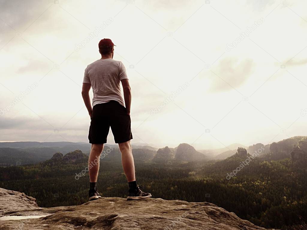 Man in t-shirt and pants. Tourist on mountain peak looking into landscape.