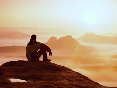 Bahar manzara. Fiyatı siyah kayalık tepe üzerinde. Harika daybreak dağlarda derin vadi ağır turuncu sis. Adam kayanın üzerinde oturup doğa mucizesi sise üzerinde
