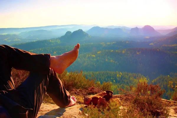 Nakna manliga håriga ben i mörk vandring byxor ta en vila på toppen av rock ovanför dalen. — Stockfoto