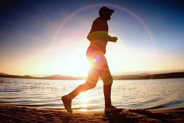 Drugie miejsce w słońcu promienie na plaży. Sportowca w czapka z daszkiem, joggingu podczas wschód słońca nad morzem — Zdjęcie stockowe