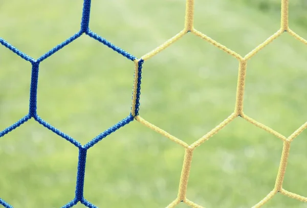 Dettaglio rete da calcio incrociata blu gialla con erba — Foto Stock