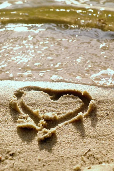 Прекрасное маленькое сердце, зарисованное соленым песком на пляже. Вечерние теплые цвета зеркала заката на уровне воды . — стоковое фото