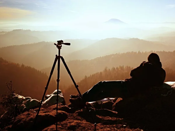 Professional photographer takes photos with mirror camera and tripod on snowy peak.