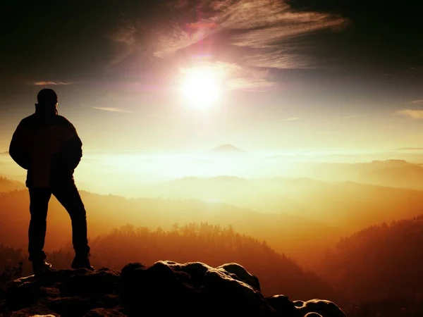 Turista alto com figura desportiva stand no ponto de vista rochoso. Colinas escuras em névoa laranja — Fotografia de Stock