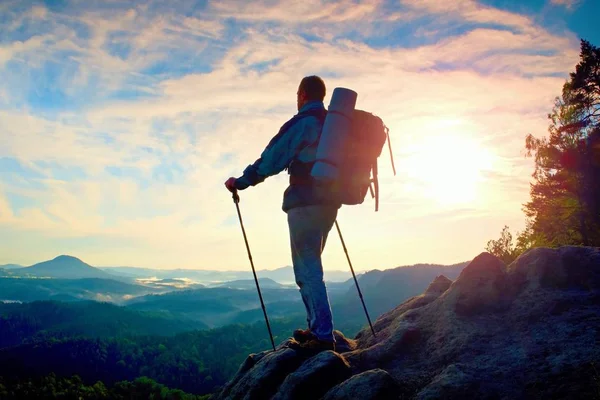 Turist guide med stolpe i handen. Vandrare med sportig ryggsäck stå på rocky synvinkel ovan misty valley. Soliga våren gryning — Stockfoto